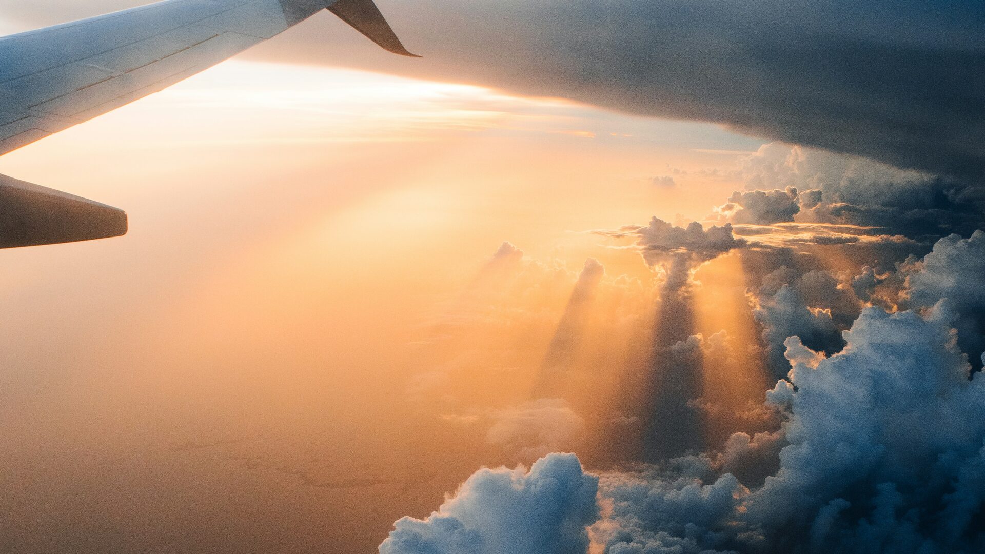 Airplane wing climbing through golden sunbeams above the clouds